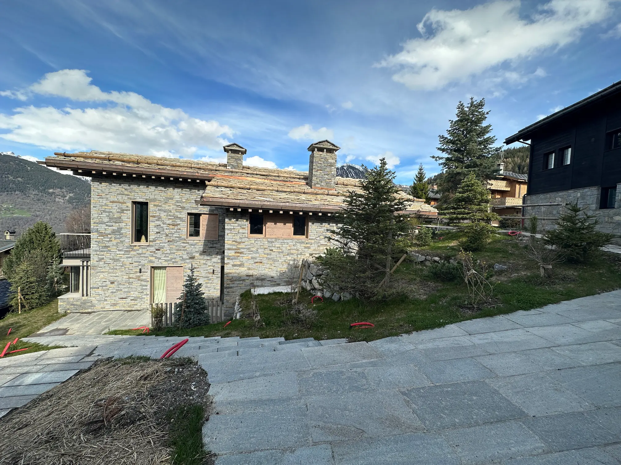 Maison en pierre avec toit en bois dans un paysage de montagne, sous un ciel bleu nuageux
